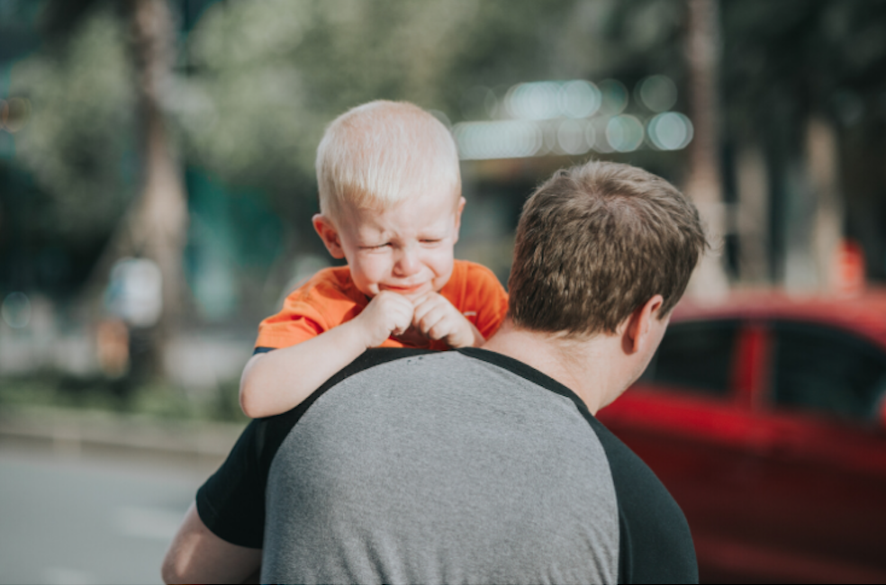 Father carrying crying child. Father is emotional coach to child.